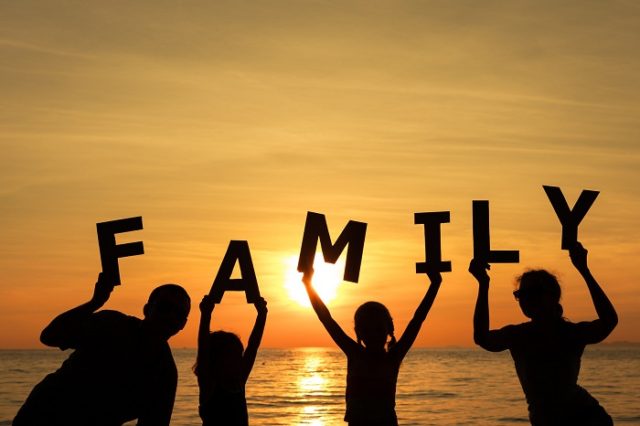 Happy family standing on the beach at the sunset time.